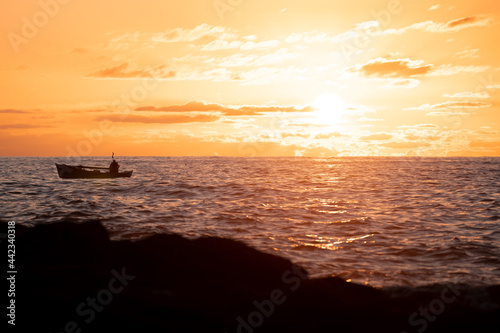 A fisherman in his boat sails the sea at sunset time with a golden sky and clouds. Concept of peace, tranquility