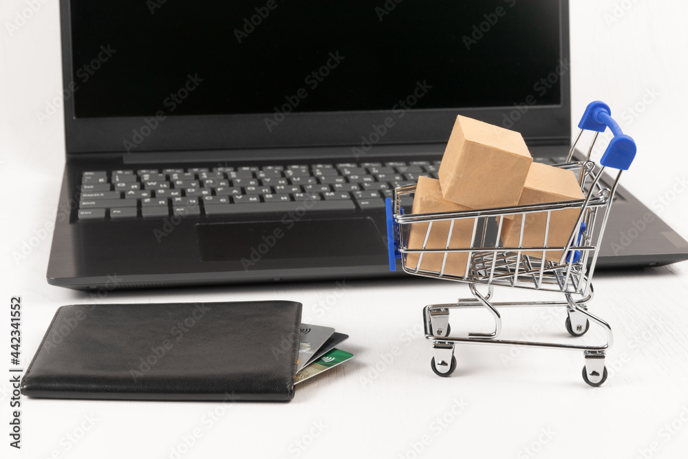 metal chrome cart with boxes and a leather wallet with bank cards on the background of a black laptop on a white wooden table. selective focus