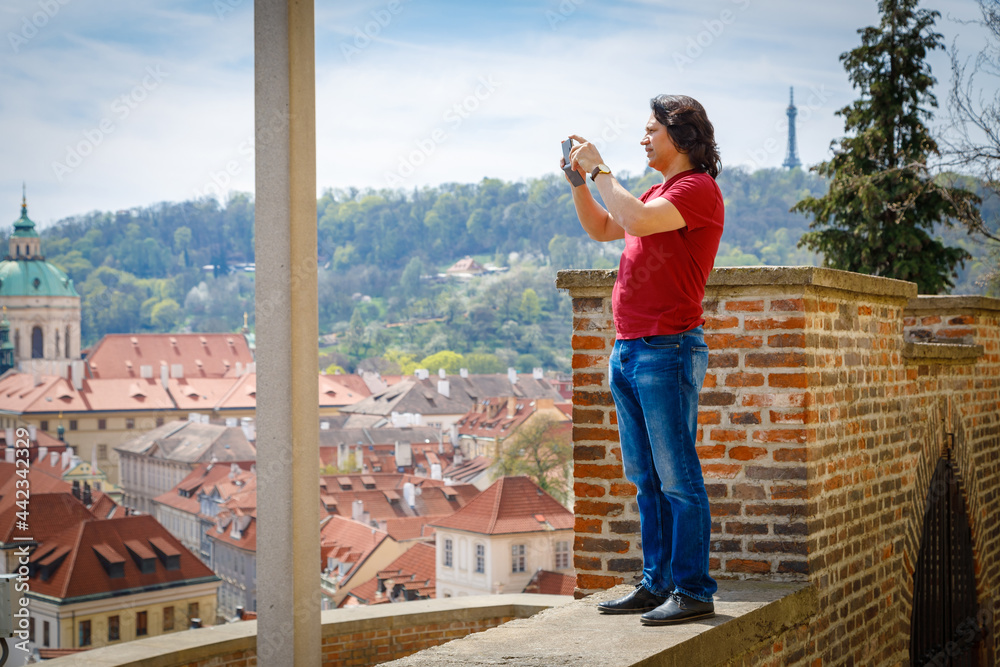 A man stands on a brick wall and photographs the panorama of Prague. Journey