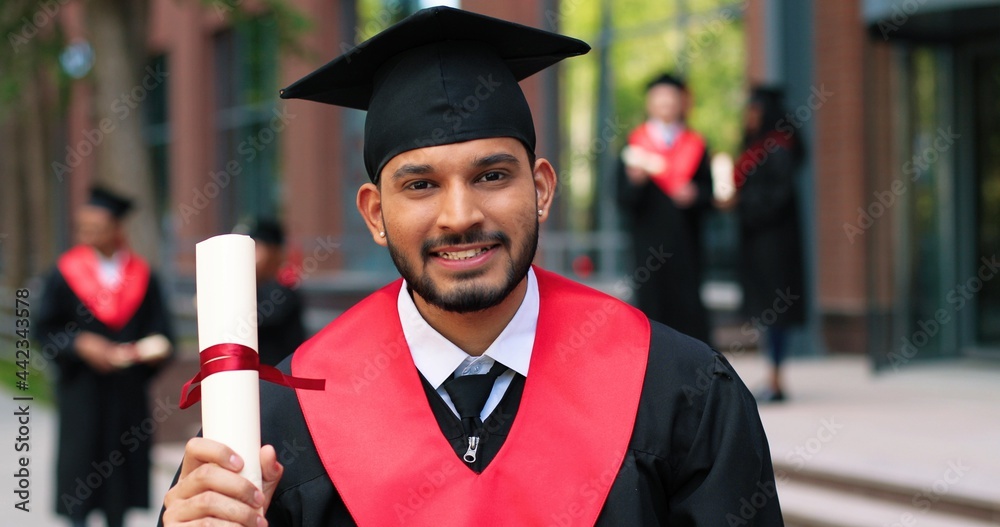 Young graduated boy holding his graduation degree convocation ceremony.  Attractive multiracial student graduate posing towards the camera during  the ceremony Stock 写真 | Adobe Stock