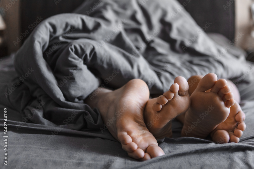 couple feet under the blanket in bed with grey sheets Stock Photo