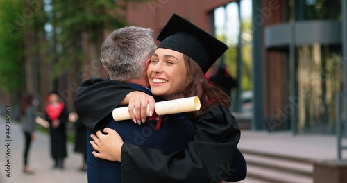 Fotografia Happy female graduate are embracing with her father with diploma at her hands and rejoicing with each other
