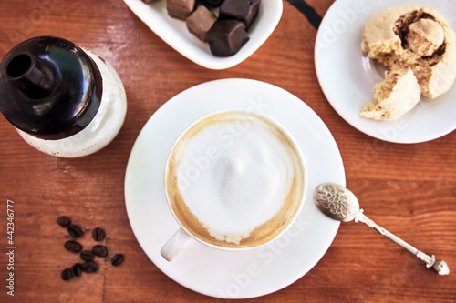 Cup of cappuccino on wooden table with cookie and chocolate.