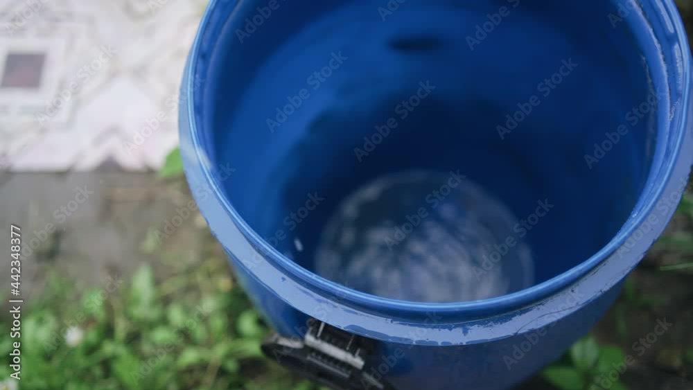It is raining and water drops fall into a plastic barrel. Shooting up