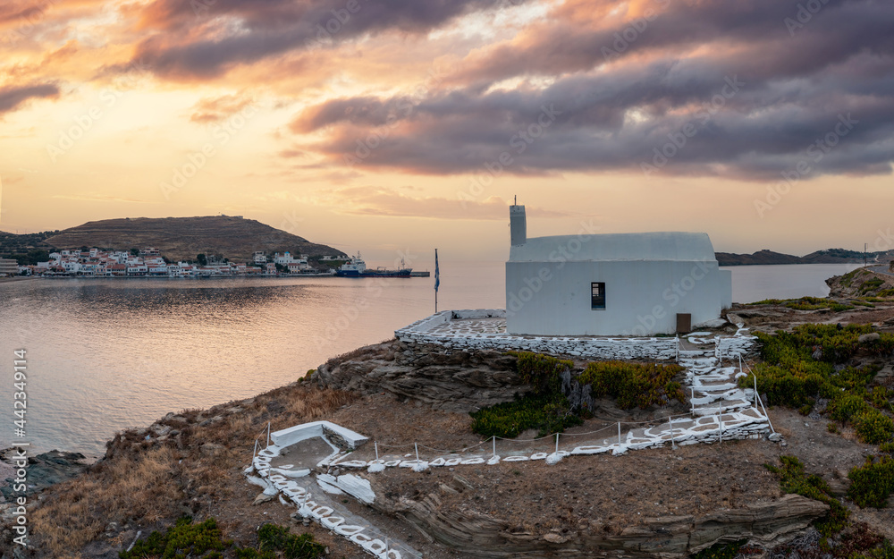 Greece, Kea Tzia island. Small white church on a rocky hill, over Korissia port at sunset