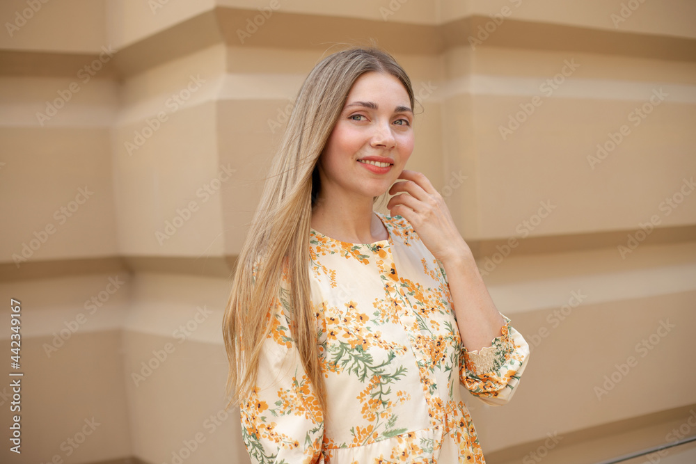 close-up of a contented caucasian woman with developing blonde hair smiling against the background of a beige wall in the street close-up of a contented caucasian woman with developing blonde hair smiling against the background of a beige wall in the street