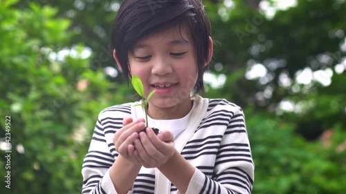 Happy Asian Child Holding Young Plant In Hands With Nature Background