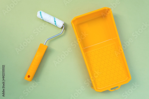 New painting roller and yellow paint tray on pastel green background