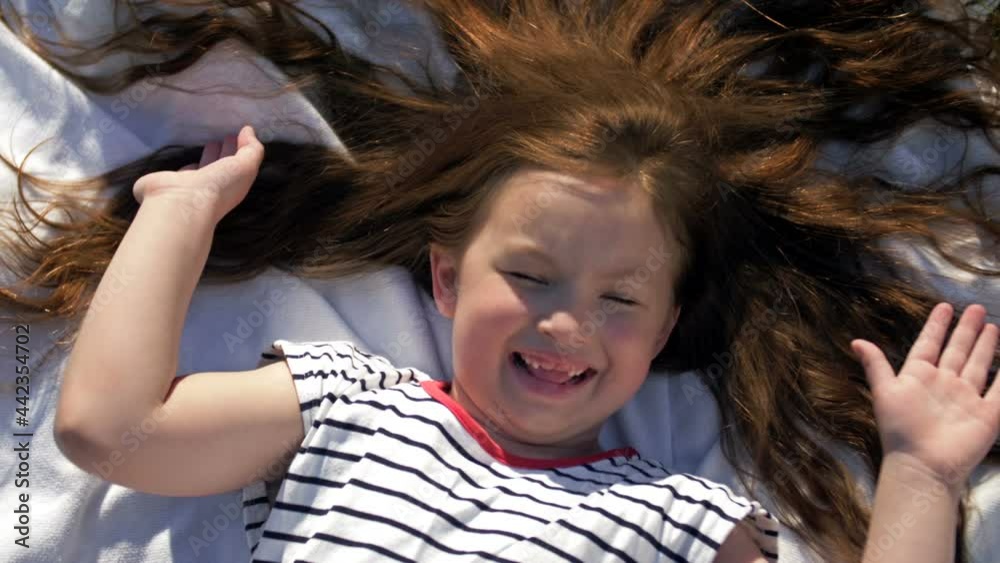Child lying on blanket having picnic in summer park. Girl spread her arms out to the sides. Child lying on blanket having picnic in summer park. Girl spread her arms out to the sides.