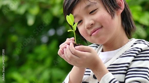 Happy Asian Child Holding Young Plant In Hands With Nature Background