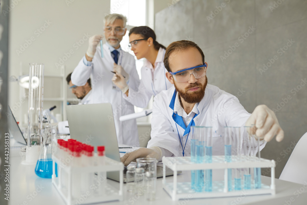 Serious male scientist, doctor or lab technician in protective goggles and gloves doing medical research, working on new vaccine and developing effective cure for diseases in modern science laboratory Serious male scientist, doctor or lab technician in protective goggles and gloves doing medical research, working on new vaccine and developing effective cure for diseases in modern science laboratory