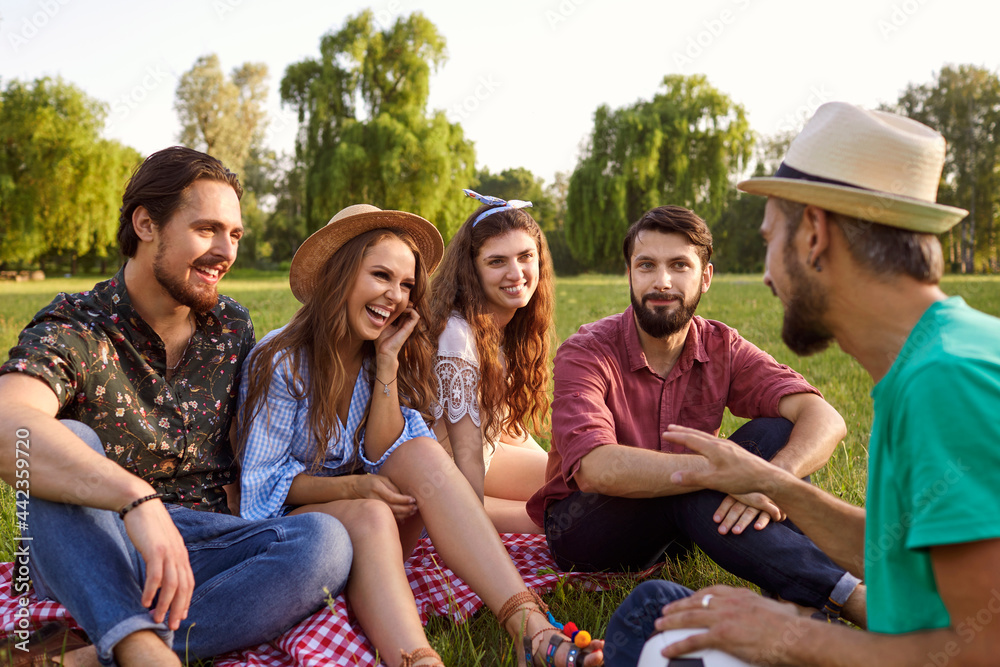 Group of young people laugh socialize talking on a picnic on the grass in a summer park. Group of young people laugh socialize talking on a picnic on the grass in a summer park.