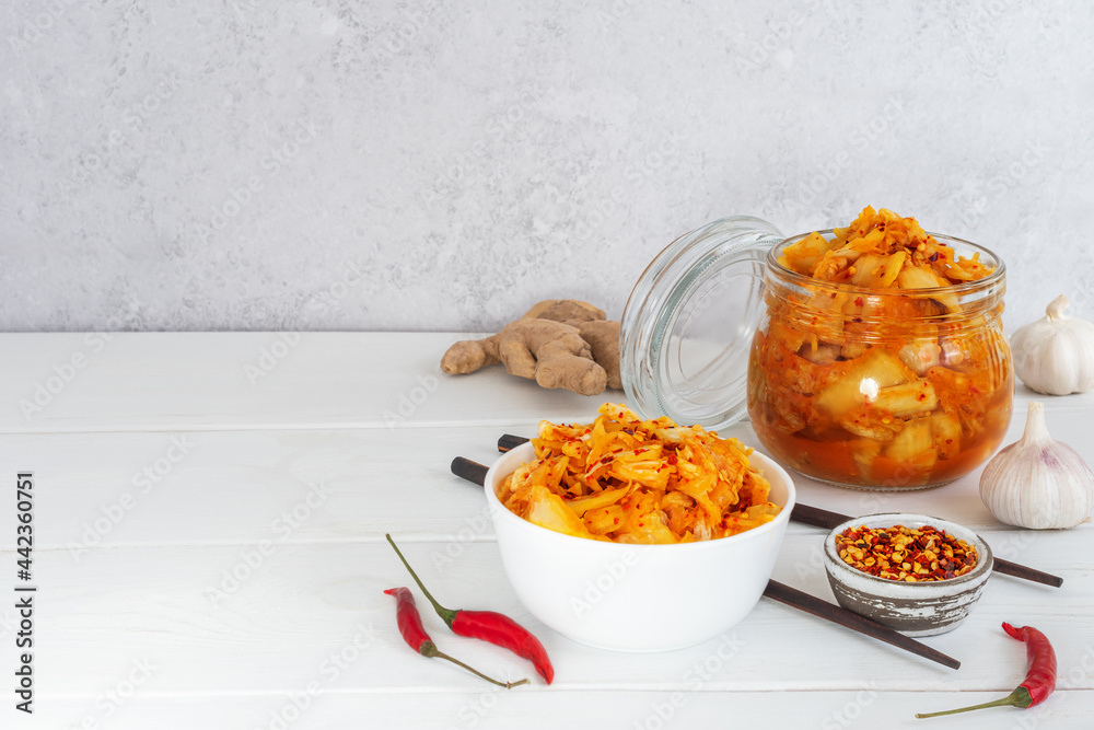 Probiotics fermented food kimchi cabbage in a glass jar and salad bowl with chopsticks on the white wooden background. Concept healthy vegetarian food. Great support the immune system. Asian cuisine. Probiotics fermented food kimchi cabbage in a glass jar and salad bowl with chopsticks on the white wooden background. Concept healthy vegetarian food. Great support the immune system. Asian cuisine.