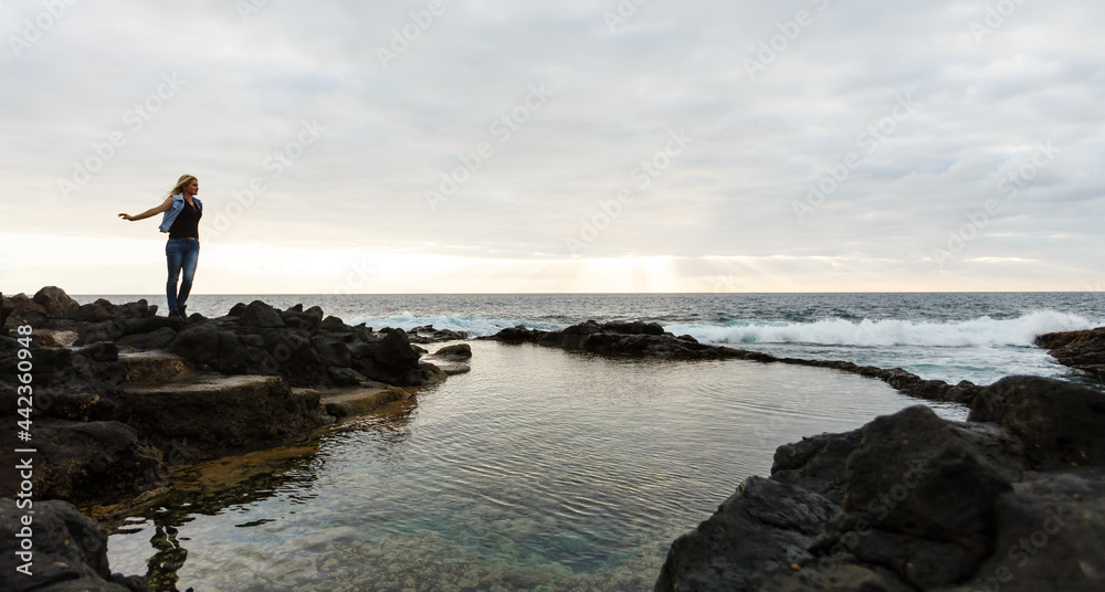 Women on volcanic rocks and blue ocean with waves, white foam and volcanic rocks. Canary Islands. The magnificent coast of the Atlantic Ocean