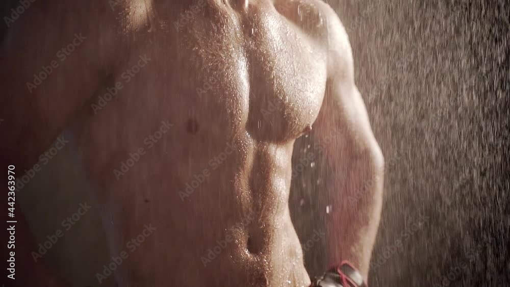 Close up body young man muscular guy bodybuilder on which water pours Portrait of Sexy Male Falling rain or shower on a dark background. Concept: sport, strong healthy body and motivation