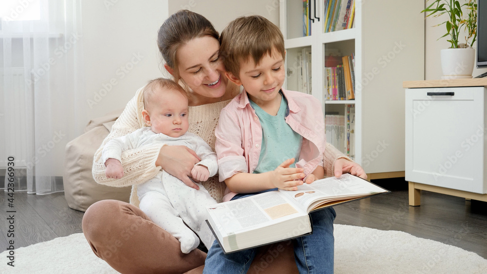 SMiling boys with young mother reading fairytale book in living room at house. Parenting, children happiness and family relationship SMiling boys with young mother reading fairytale book in living room at house. Parenting, children happiness and family relationship