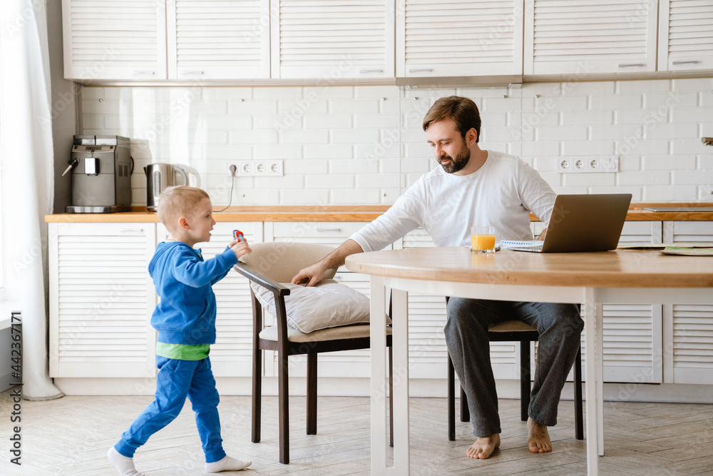 Fototapeta premium White father playing with his son and using laptop in kitchen