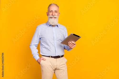 Photo of attractive cute age gentleman wear blue shirt standing holding modern device empty space isolated yellow color background