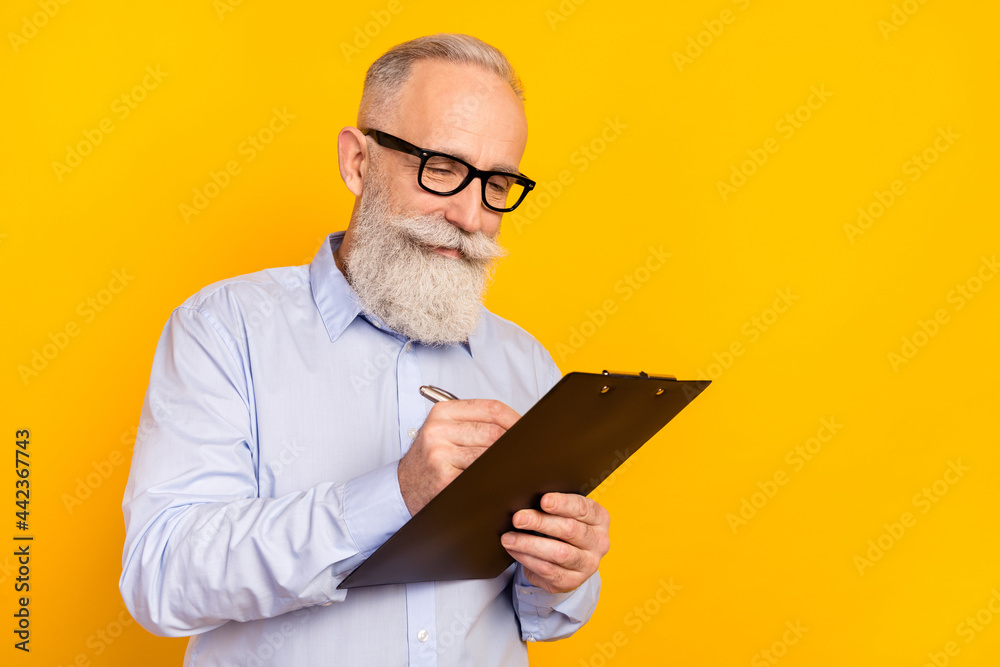 Photo of excited confident mature man dressed formal outfit spectacles writing clipboard isolated yellow color background