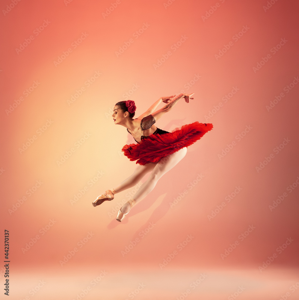 Young and incredibly beautiful ballerina is posing and dancing at red studio full of light.