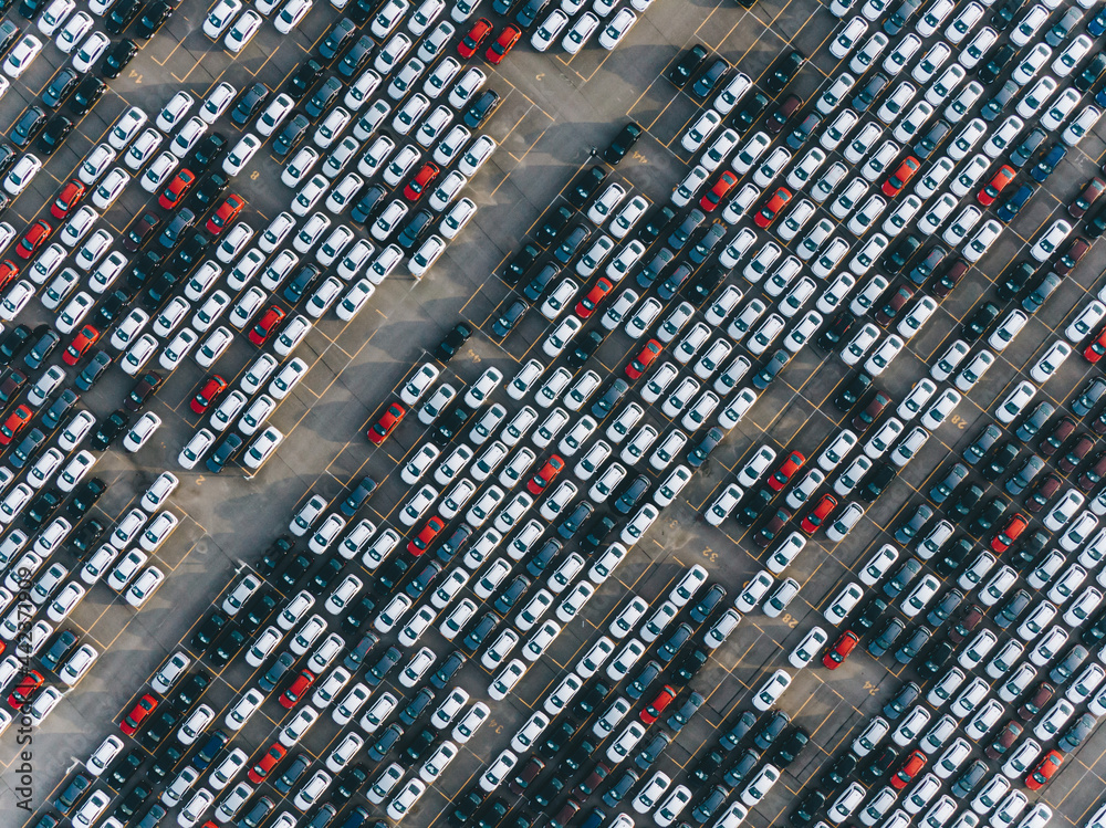 New multi-colored passenger cars are standing in straight diagonal rows in a giant parking lot on the territory of the plant, aerial view