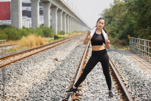 Asian young woman tan skin in black sportswear outdoor physical exercises for successful health at railway side and eye contact to camera. © eakgrungenerd