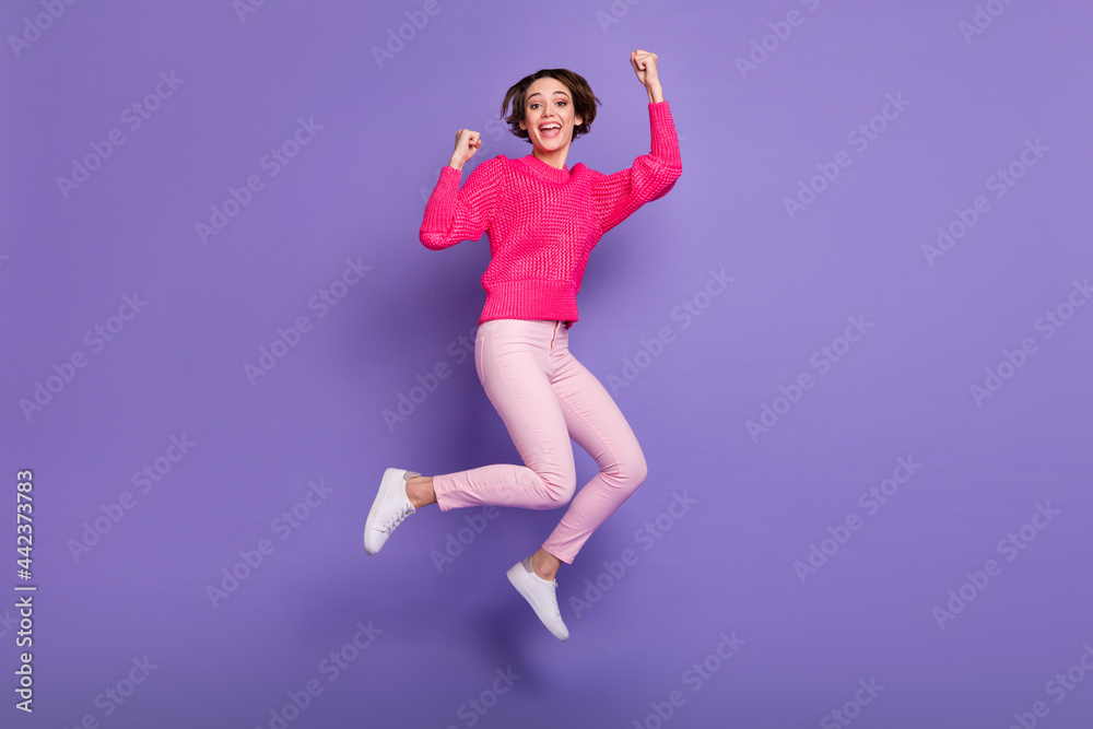 Full body photo of young girl happy celebrate win victory jump up wear pants fists hands isolated over purple color background