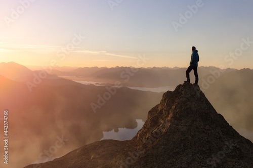 Adventure Composite. Adventurous Adult Man hiking on top of a mountain. Colorful Sunset or Sunrise Sky. 3D Rocky Peak. Aerial Background Landscape from Vancouver Island, British Columbia, Canada. photo