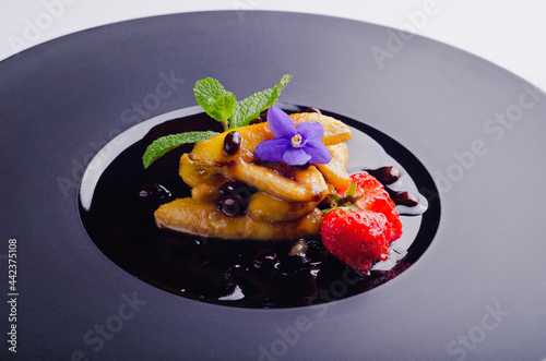 Delicious dessert with fried banana. Delicious dessert with violet flower. Vacation sweet delight. Coffee syrup