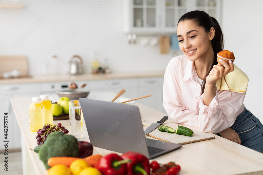 Smiling woman watching movie using laptop and eating dessert