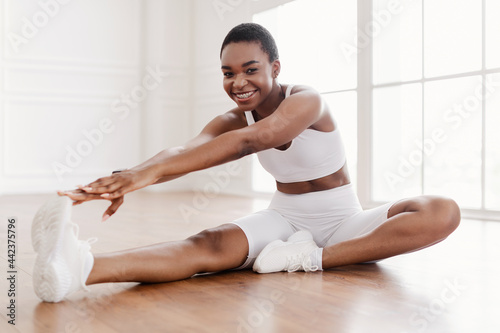 Fotografi Cheerful Black Woman In Sportswear Stretching Leg On Floor