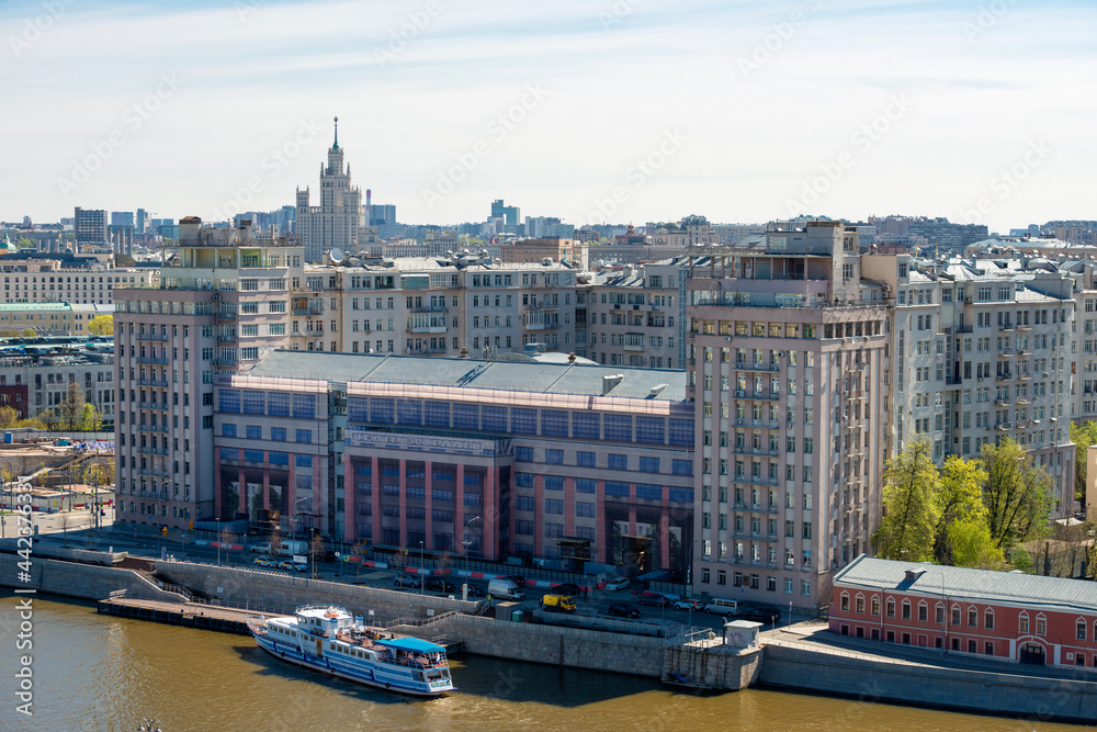 Obraz premium Top view of a house on the embankment on Berezhkovskaya embankment with the Estrada theater and a pleasure boat at the pier of the Moskva River on a spring day