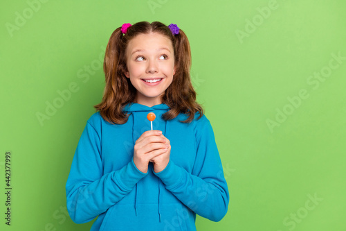 Photo of happy dreamy young small girl hold hand candy look empty space isolated on green color background