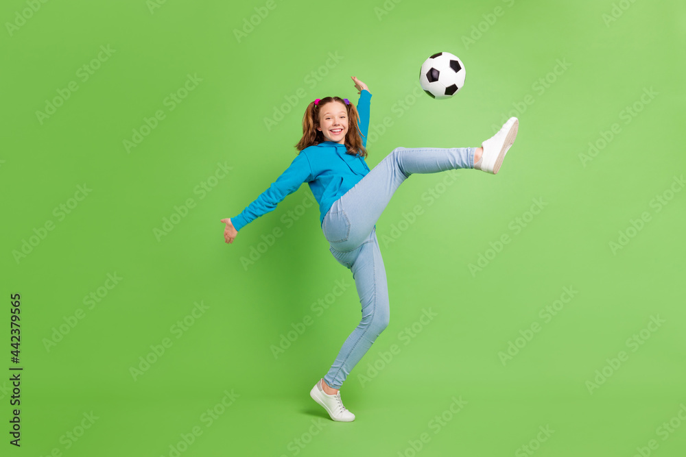 Full length photo of happy nice young little girl play soccer good mood kick isolated on green color background Full length photo of happy nice young little girl play soccer good mood kick isolated on green color background