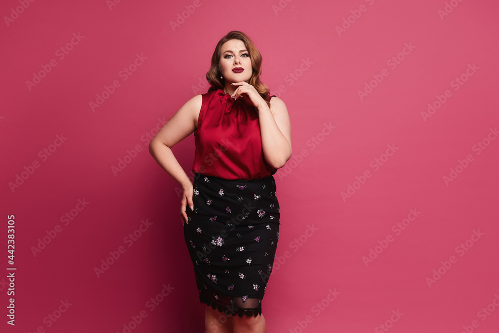 Young plus size caucasian model woman in red satin blouse and skirt posing over pink background. Gorgeous plump woman in modish outfit over pink background Young plus size caucasian model woman in red satin blouse and skirt posing over pink background. Gorgeous plump woman in modish outfit over pink background