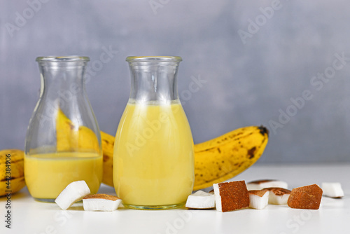 Two jars with yellow banana and coconut smoothie drink in jar next to ingredients