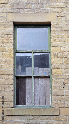 boarded up window with broken panes in an old abandoned house with stone walls and green frame