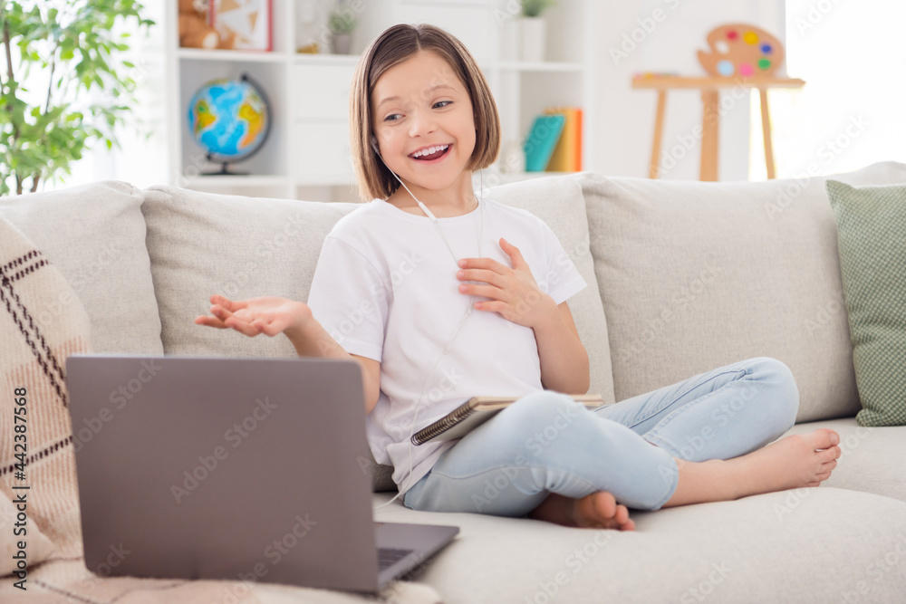 Photo of shiny impressed small schoolgirl dressed white t-shirt sitting coach video call modern gadget indoors room home house Photo of shiny impressed small schoolgirl dressed white t-shirt sitting coach video call modern gadget indoors room home house