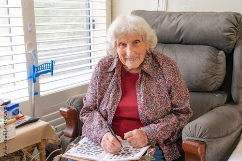 An elderly lady sitting in a chair doing a crossword and smiling
