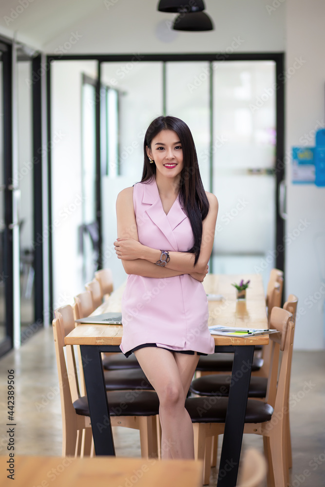 Asian businesswoman in a pink dress stands with her arms crossed looking at the camera at the office. Asian businesswoman in a pink dress stands with her arms crossed looking at the camera at the office.