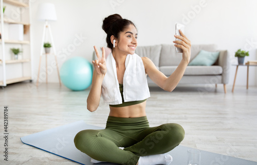 Joyful Indian woman taking selfie on break from home workout, full length