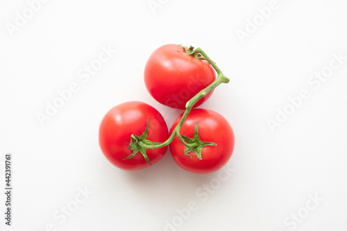 Three red tomatoes connected by a green branch. View from above