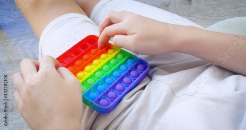 Child is playing trendy popular board game anti-stress toy pop it. Multi-colored popular silicone anti-stress toy pop it.