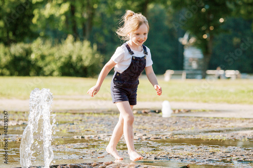 Obraz na płótnie Cute cheerful girl playing in fountain. Kid in denim overall having fun in summer park w salonie