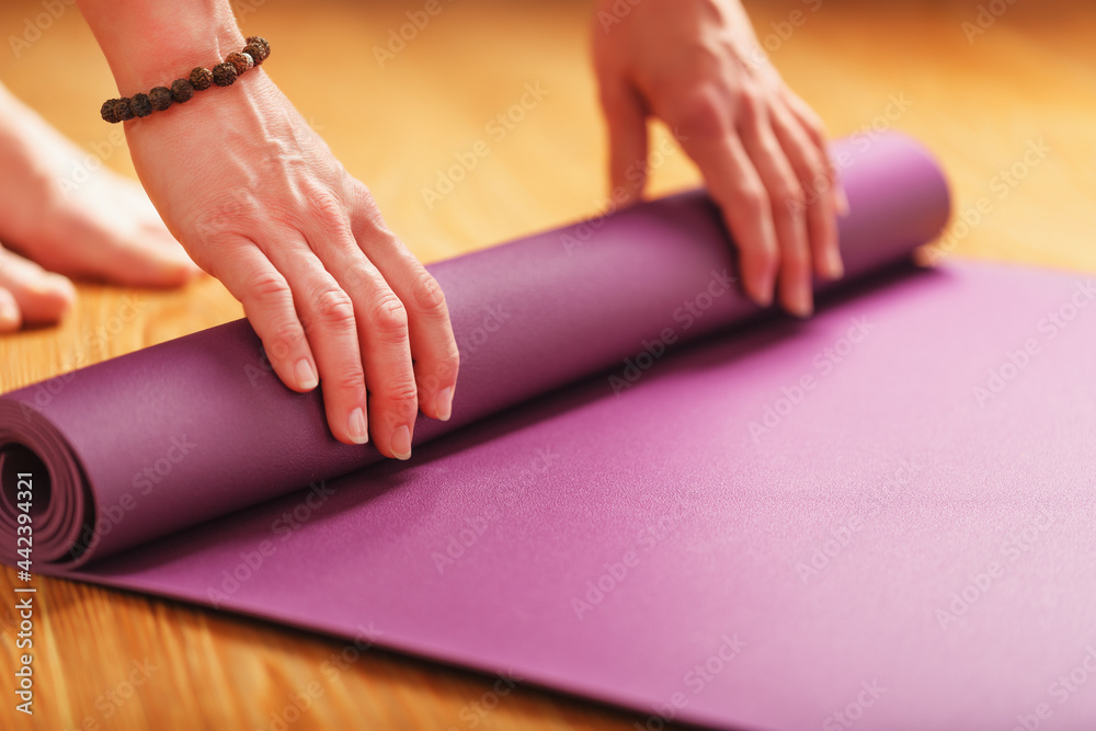 A girl lays out a lilac yoga mat before a workout practice at home on a wooden floor.