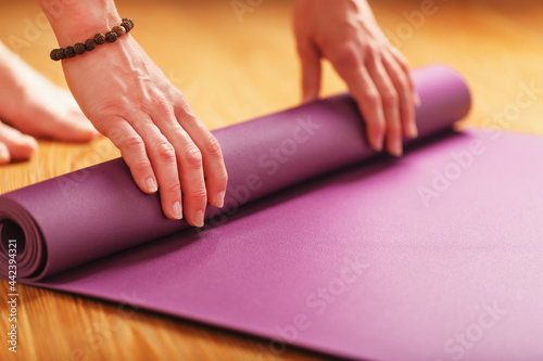 A girl lays out a lilac yoga mat before a workout practice at home on a wooden floor.