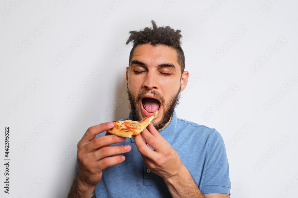 Human holds piece of cheese pizza with tomatoes in his hands and enjoys eating. Young cute Caucasian man with beard and dreadlocks eats pizza on white neutral background. Horizontal banner. Human holds piece of cheese pizza with tomatoes in his hands and enjoys eating. Young cute Caucasian man with beard and dreadlocks eats pizza on white neutral background. Horizontal banner.