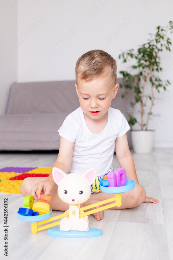 cute baby boy plays with scales at home on the floor trying to balance them, the concept of early development of children