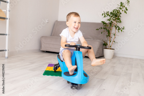 a cheerful child boy rides a blue car at home with an orthopedic rug on the floor