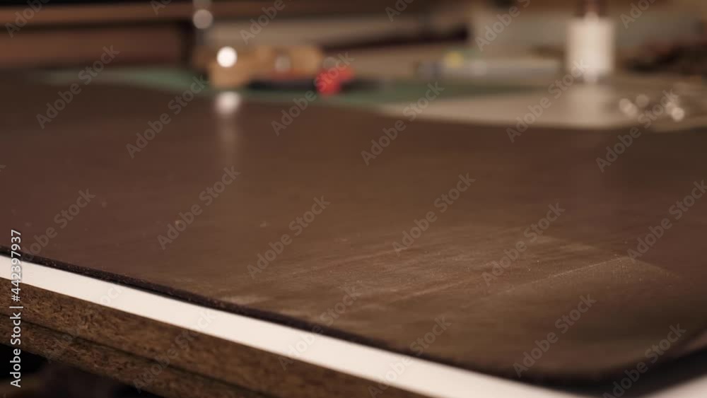 Leather worker untwisting a roll of leather on a table in a workshop. Side view of a master working with leather. Man touching a piece of leather on the table in the workshop Leather worker untwisting a roll of leather on a table in a workshop. Side view of a master working with leather. Man touching a piece of leather on the table in the workshop